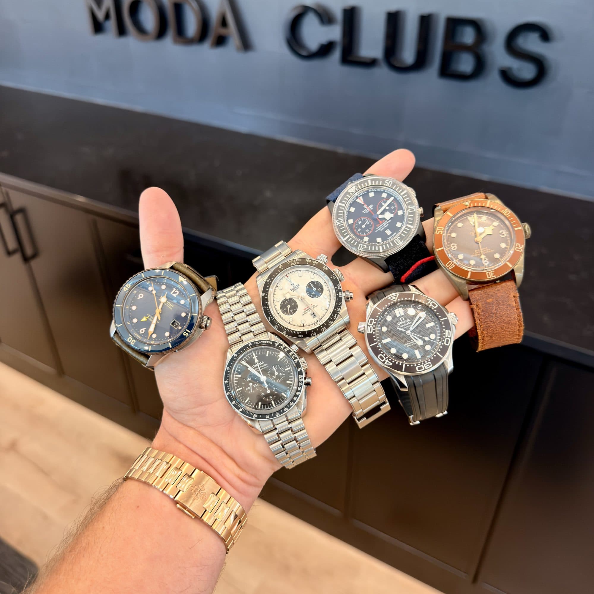 Vadim holding the six starting watches in one hand in front of the Moda Clubs sign: a Bremont, two Omegas and three Tudors