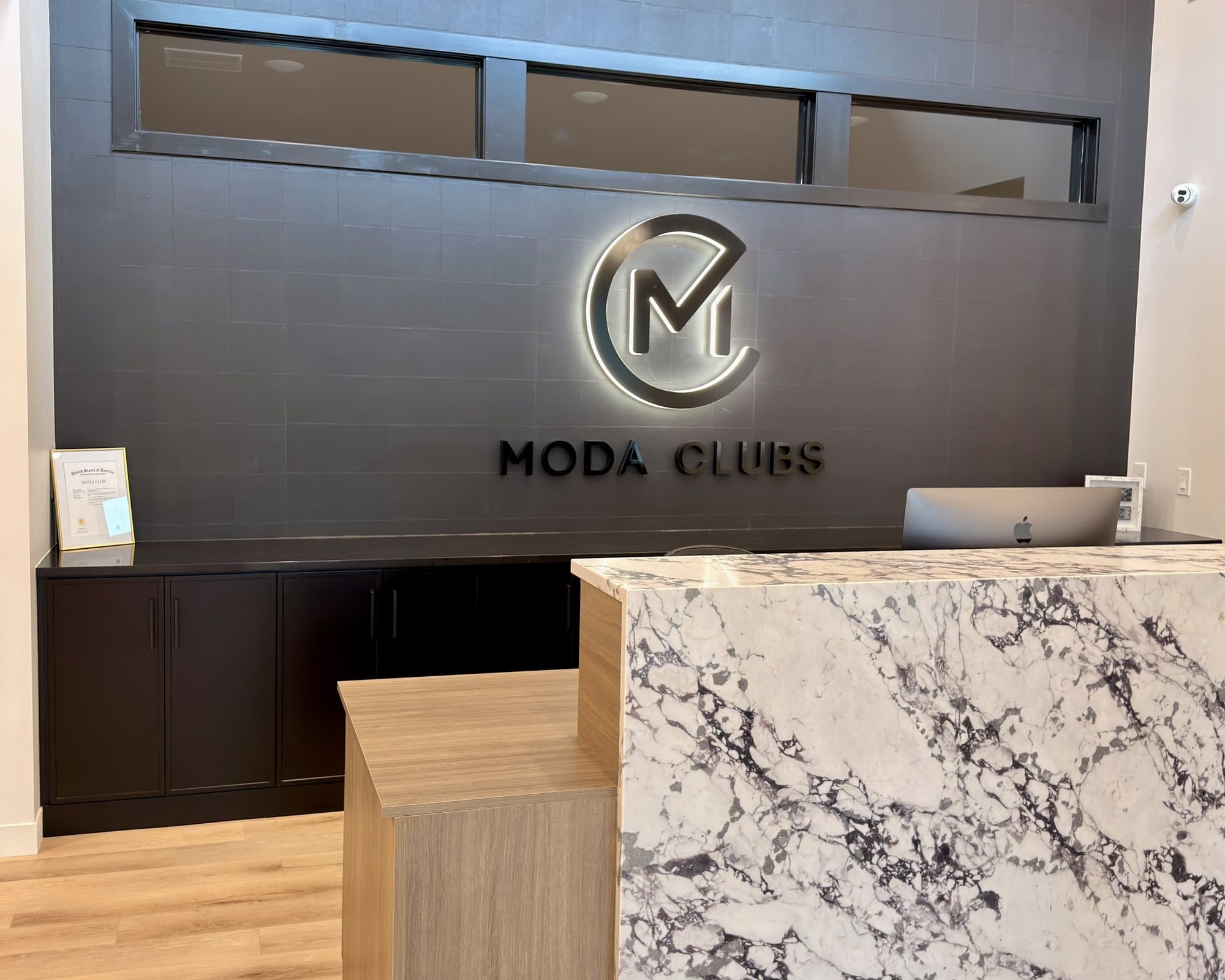 The front desk at Moda HQ in Sioux Falls, with a backlit Circle M logo and the words Moda Clubs on a dark wall