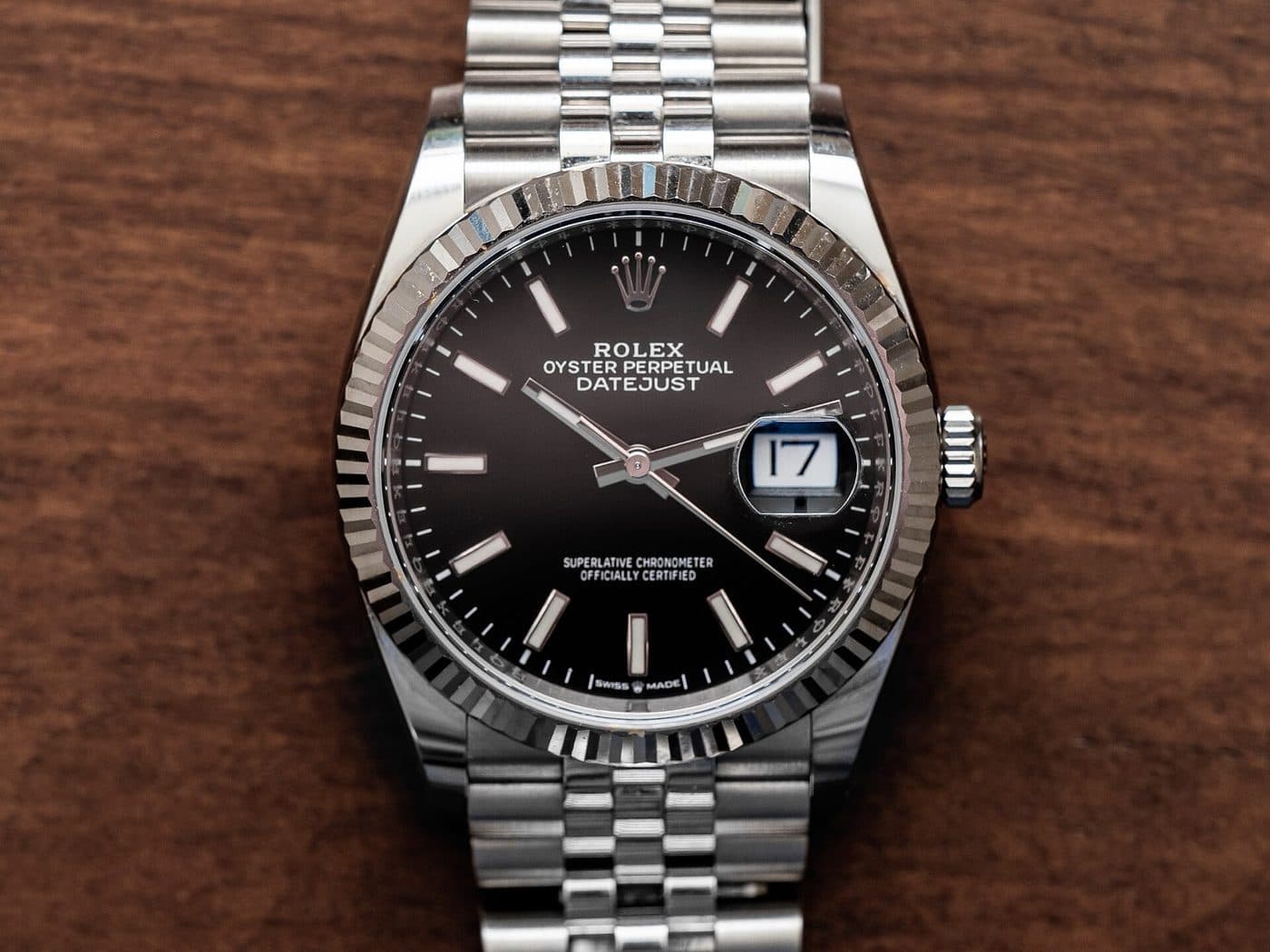A steel Rolex Datejust 36 with a black dial and fluted bezel on a Jubilee bracelet, lying on a wooden table