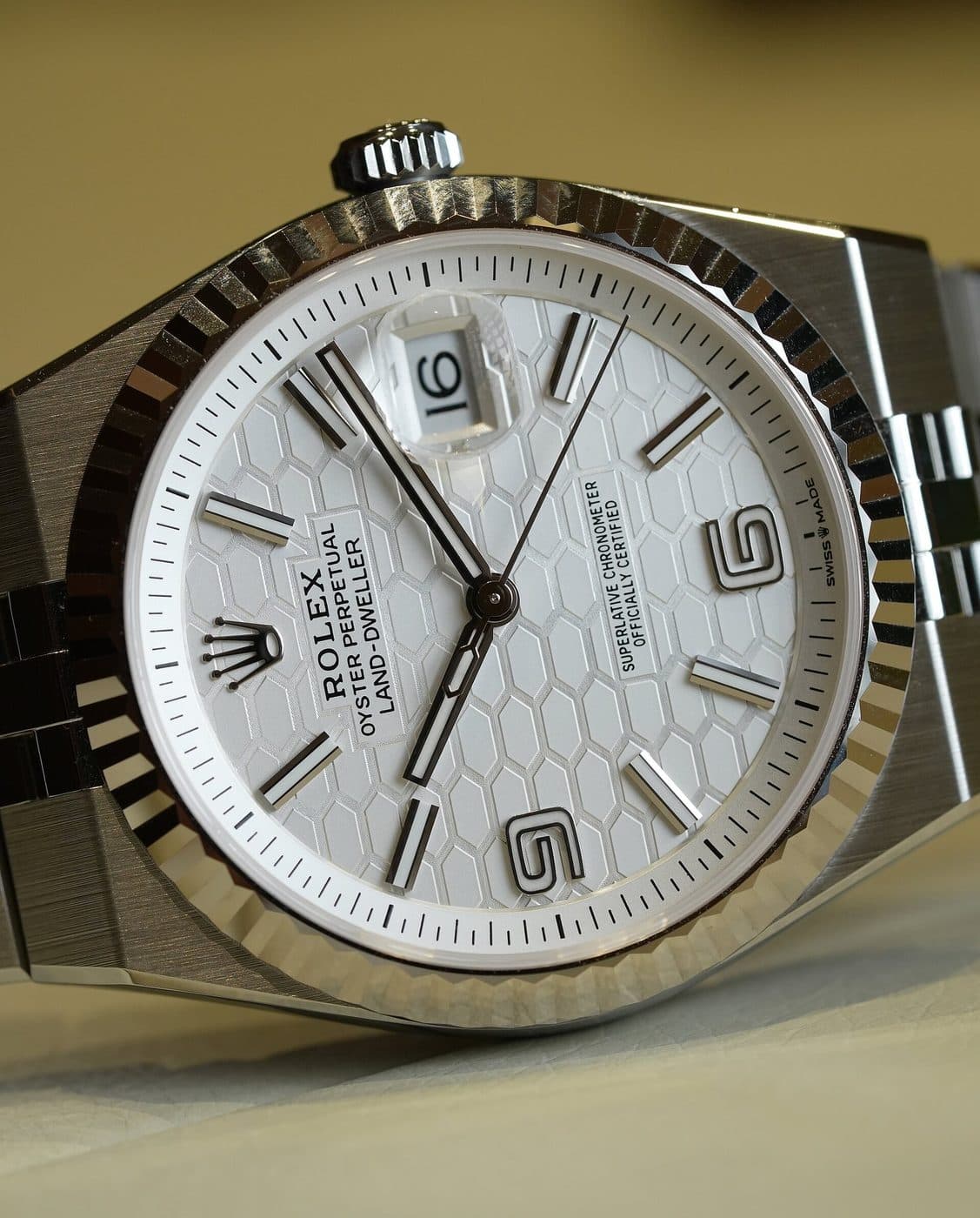 Close-up of a steel Rolex Land-Dweller with a fluted bezel and white dial, showing where the flat bracelet joins the case