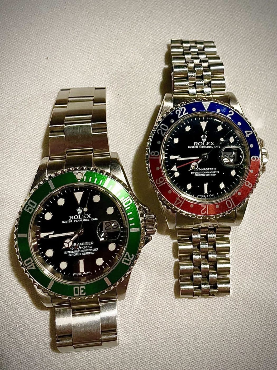 A Rolex Submariner with a green bezel on a three-link Oyster bracelet beside a GMT-Master II with a blue and red bezel on a five-link Jubilee bracelet