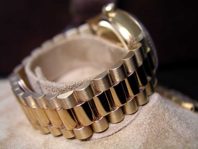 Side view of a yellow gold Rolex President bracelet wrapped around a suede watch cushion, showing its rounded three-piece links