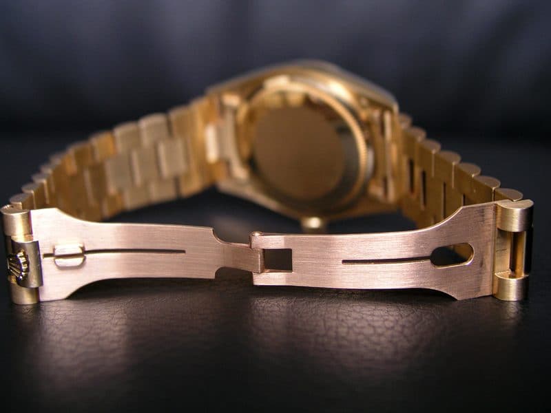 The back of a yellow gold Rolex Day-Date on a President bracelet, with the concealed clasp open to show its two folding blades