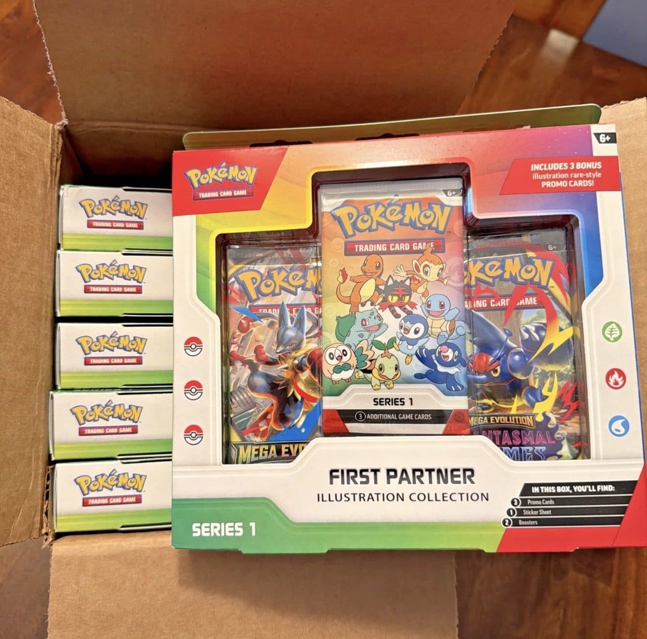 A sealed Pokemon First Partner Illustration Collection box and five sealed Pokemon boxes packed in a shipping carton, from KWE2x inventory