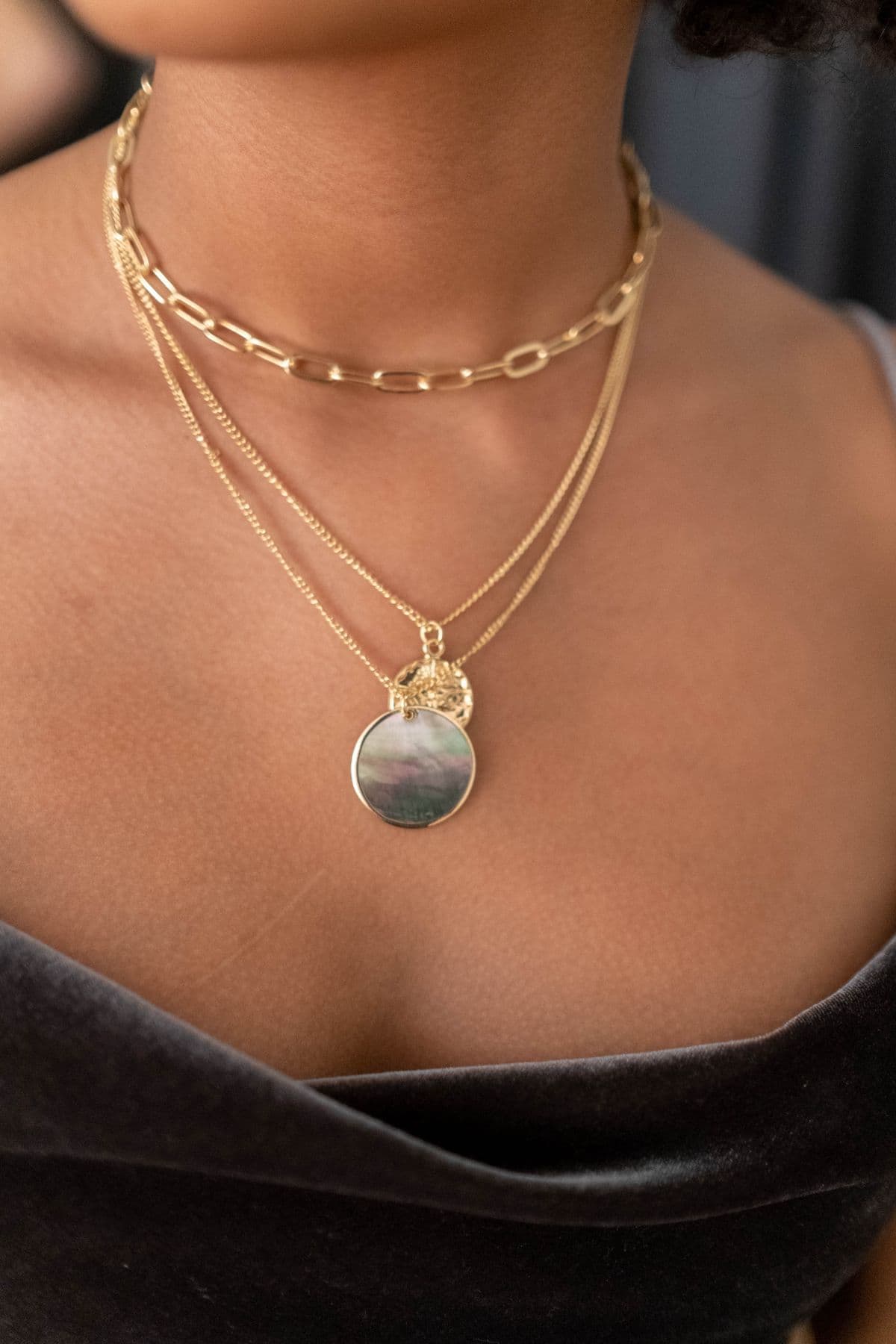 Layered gold necklaces on a dark velvet shoulder, representing the fine jewelry traded inside Moda Gold+.