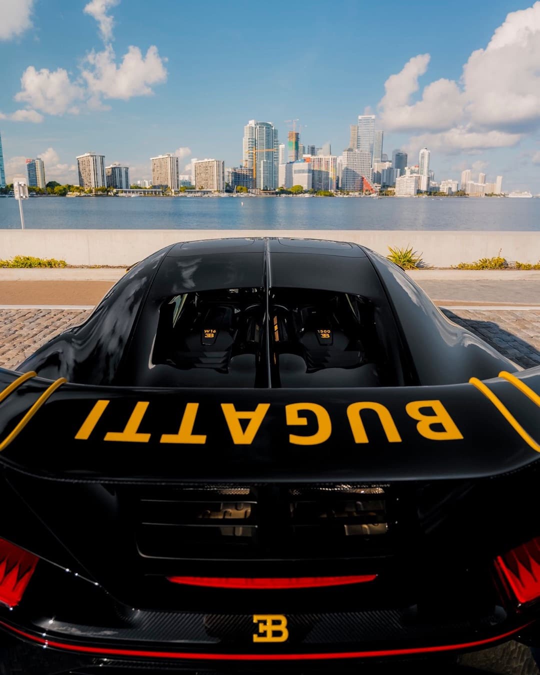 A black Bugatti with gold lettering parked across the water from the Miami skyline