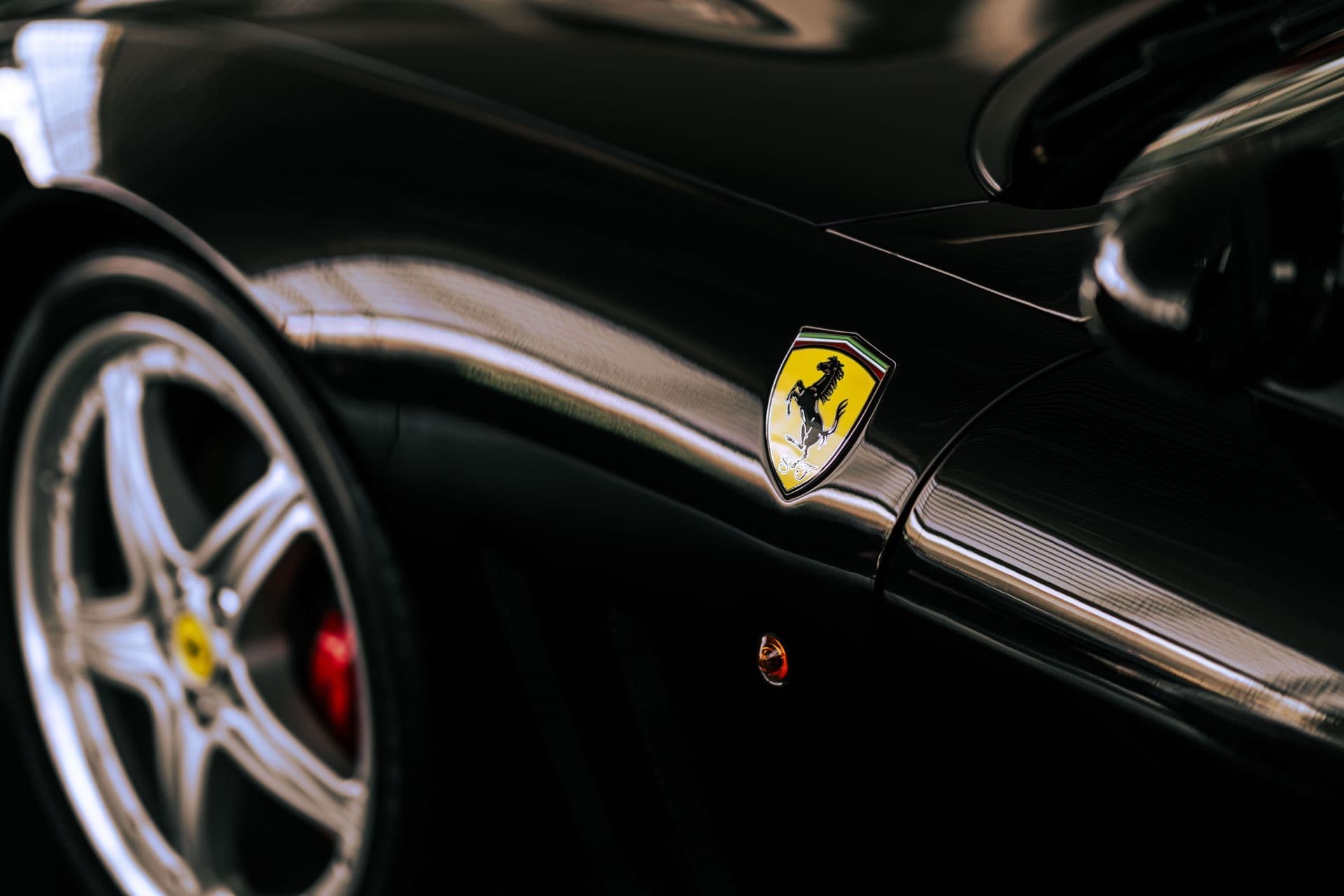 A glossy black Ferrari, close on the emblem and front wheel