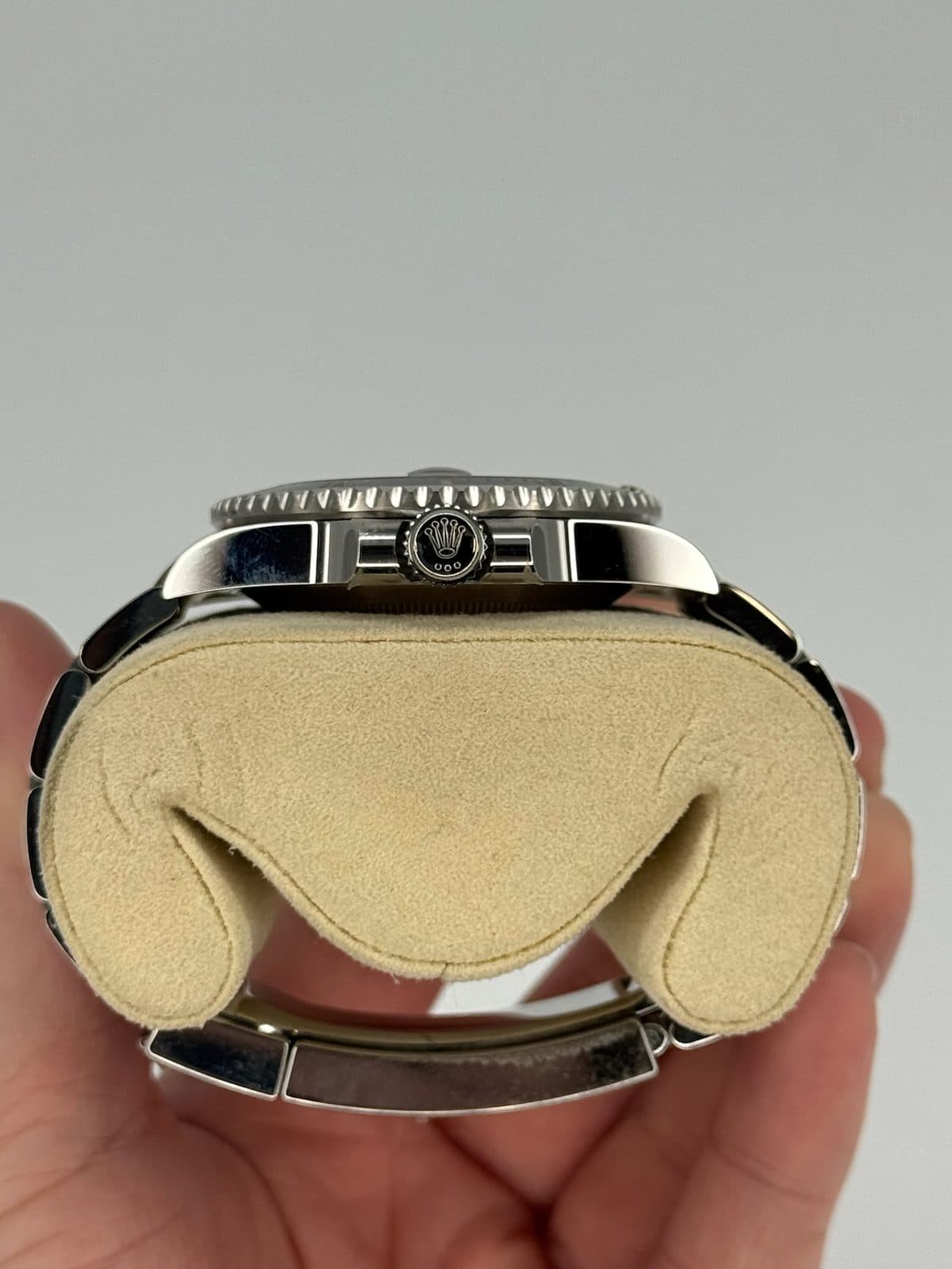The crown side of a Rolex Submariner 116610LN case on a watch pillow, showing the screw-down crown between its crown guards