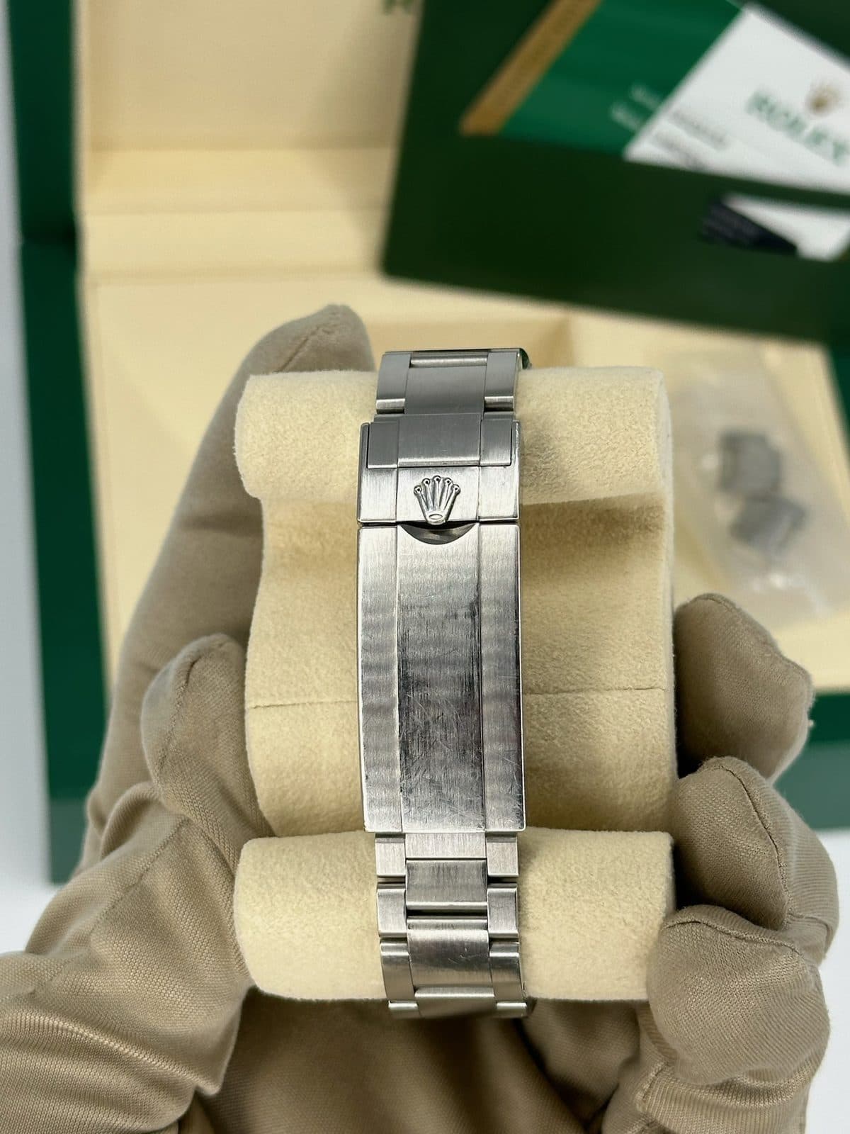 The closed Oysterlock clasp of a Rolex Submariner 116610LV on a watch pillow, with the box and a bag of spare links behind