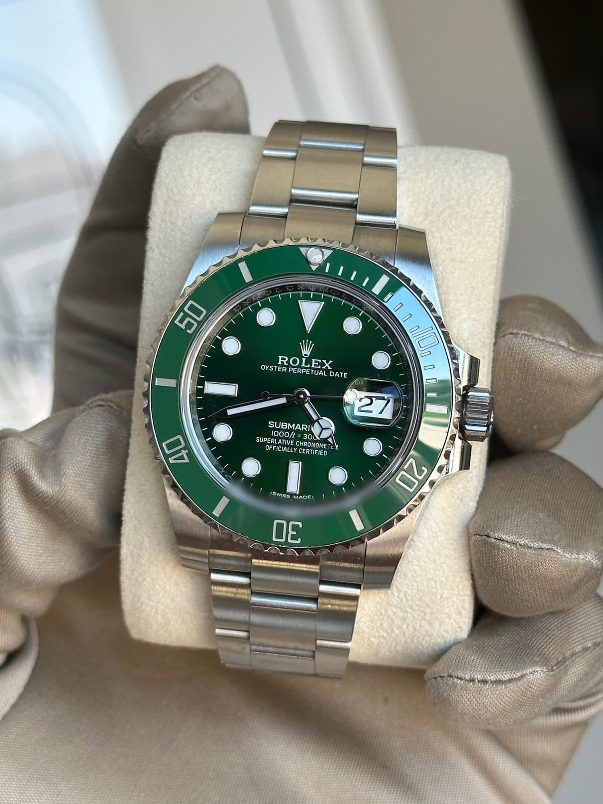 Rolex Submariner Date 116610LV with its green sunray dial and green Cerachrom bezel, held upright on a watch pillow