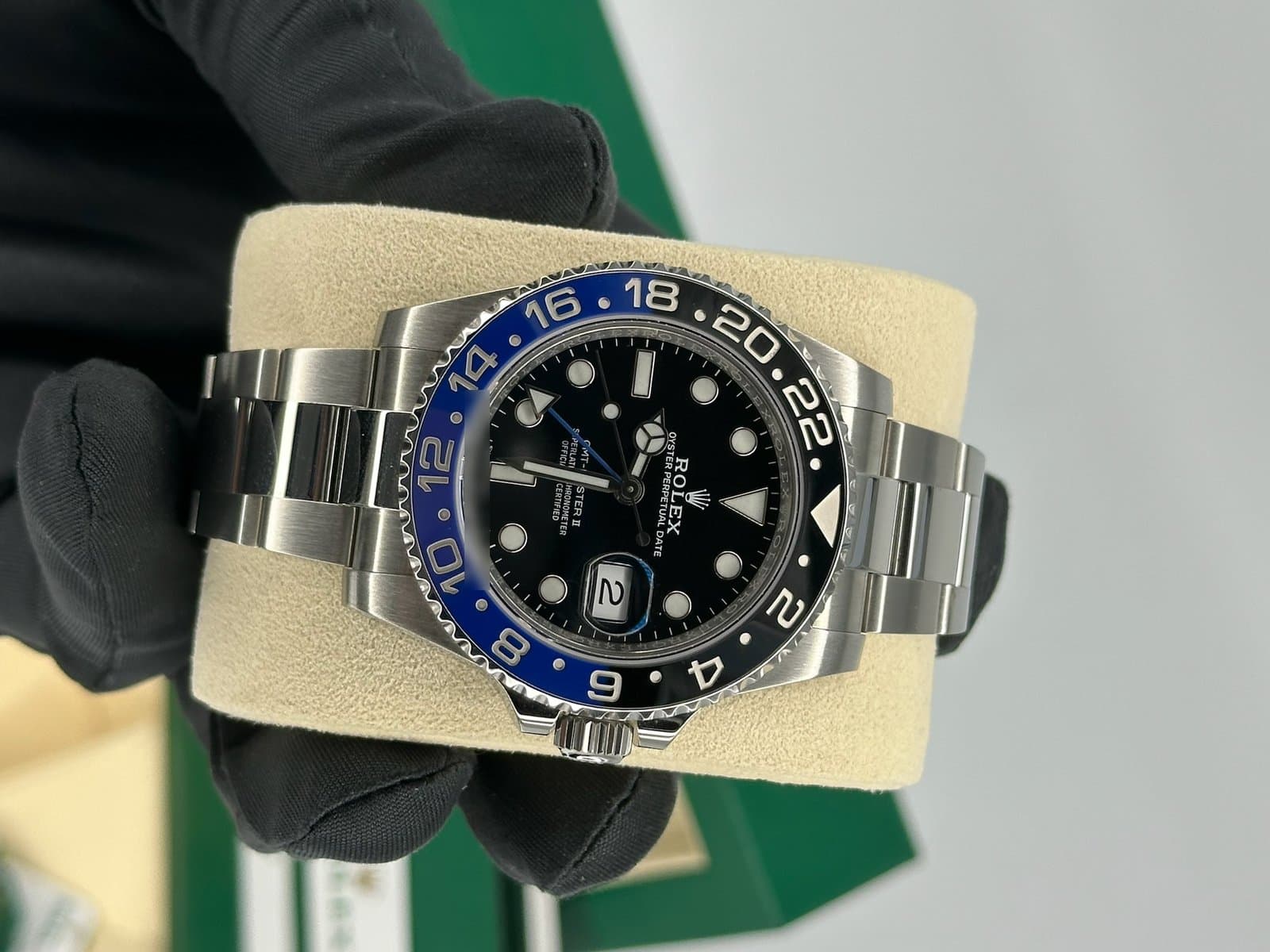 Rolex GMT-Master II 116710BLNR with a black dial, blue 24-hour hand and blue and black ceramic bezel, on a cream watch pillow held in a black-gloved hand